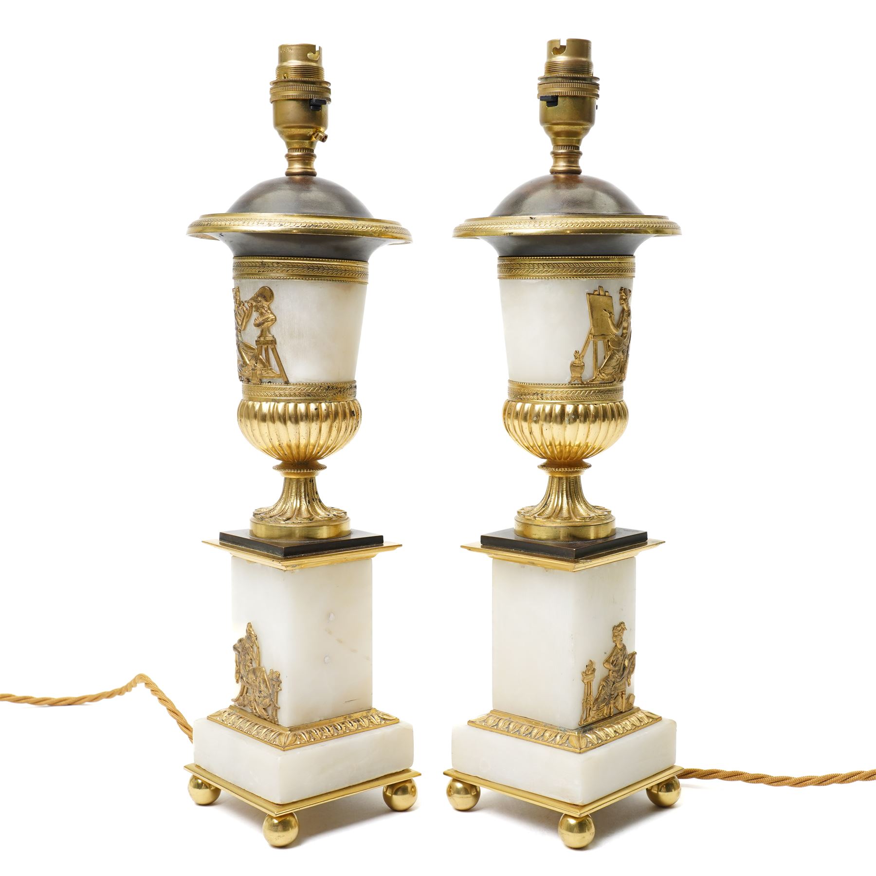 Pair of early 20th-century Neoclassical lamp bases in gilt bronze and alabaster, each decorated with classical figural reliefs celebrating the arts, each of baluster form, the alabaster bodies applied with finely cast gilt-bronze scenes including a seated painter at an easel, a sculptor at work, and allegorical female figures with musical  and theatrical motifs, mounted on square alabaster plinths with gilt-bronze borders and raised on bun feet, the domed shoulders enriched with laurel-leaf mouldings, H42cm 