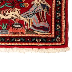 Two small rugs, an ivory ground example decorated with a central floral medallion and scattered rose sprays, enclosed by a navy foliate border (62cm x 101cm), and a crimson pictorial mat worked with seated figures, an animal and birds amongst flowering plants (45cm x 79cm) (2)