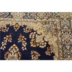 South East Persian Kirman hand-knotted carpet, indigo blue field with central floral medallion in tones of ivory, indigo,  and soft blue, issuing network of scrolling vinery, palmettes and floral sprays, conforming spandrels, broad main border of scrolling foliage and stylized palmettes, framed by multiple guard borders, with cotton fringe ends 