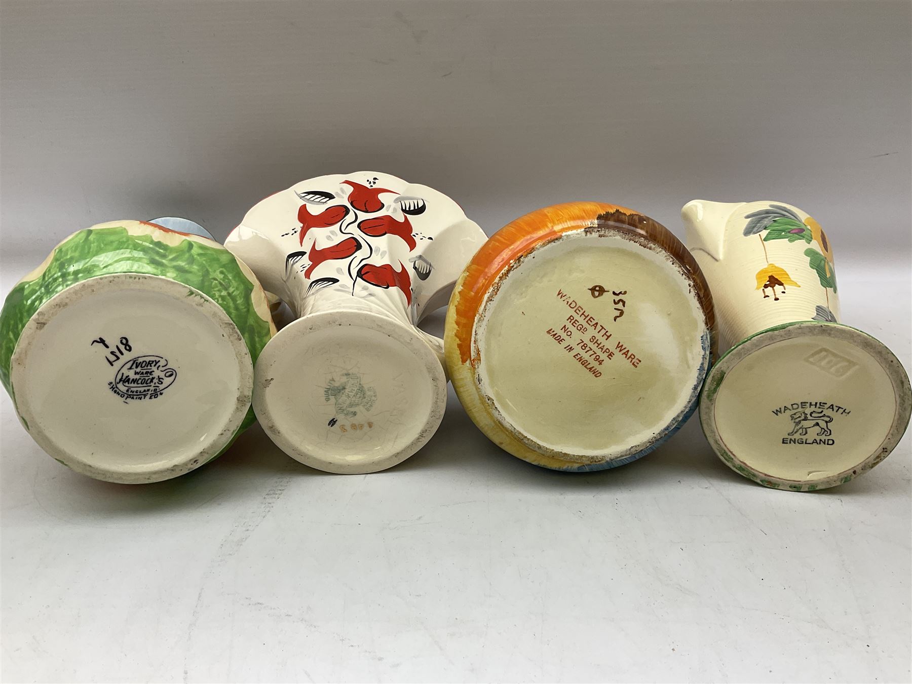 Group of Art Deco ceramics, comprising Wadeheath jug painted in spiralled bands of blue, orange, yellow and brown, shape no. 707784, Royal Doulton Caprice pattern twin handled bowl, no. D5358, Arthur Wood wall pocket of typical stylised fan form with painted floral decoration, Arthur Wood vase of cornucopia form with red and grey floral decoration, Wadeheath jug of ribbed form with stylised handle, and two Hancock's Ivory Ware jugs, tallest example H26cm