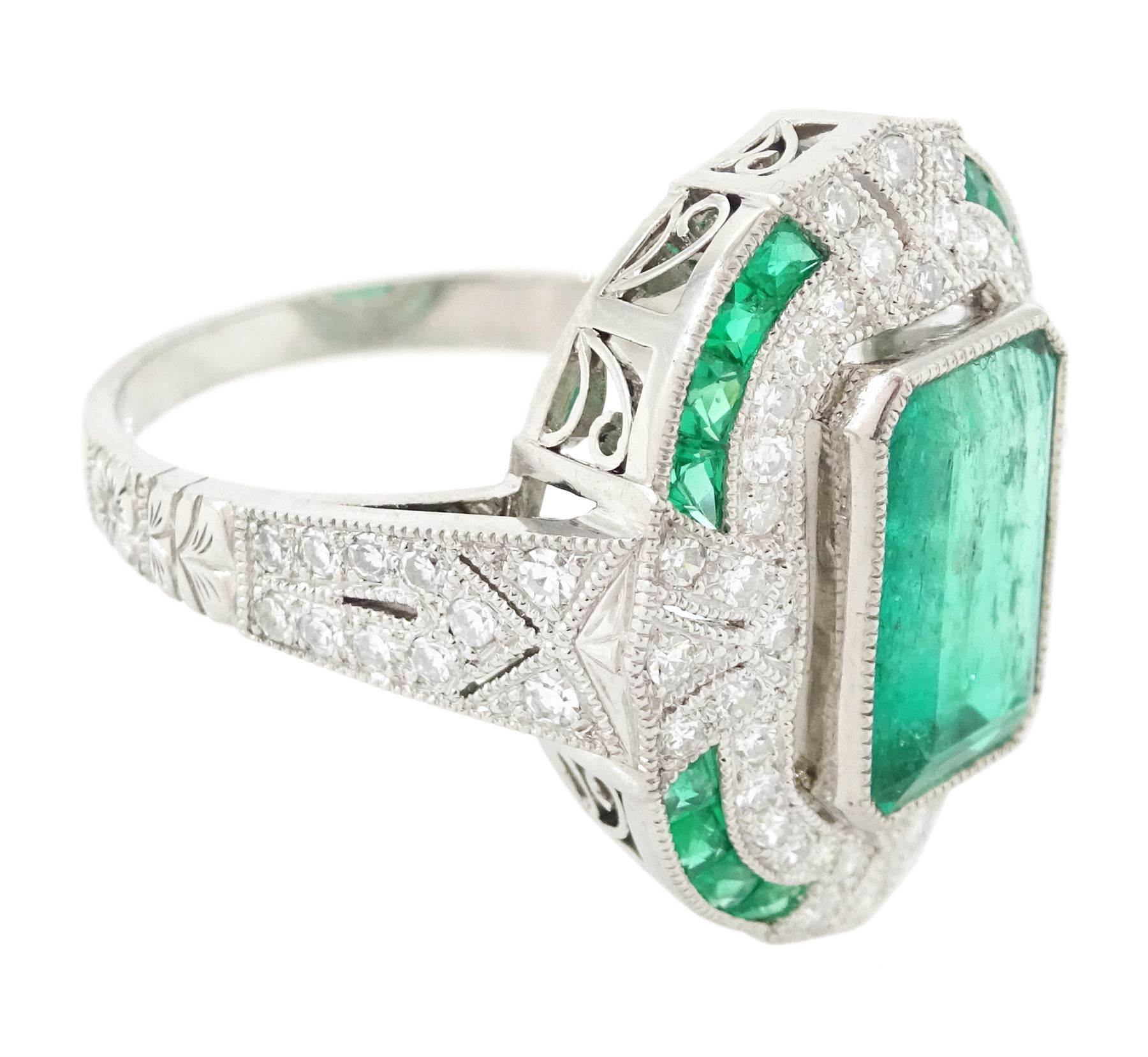 Platinum emerald and diamond milgrain set dress ring, single octagonal cut emerald of 2.40 carat, surrounded by single cut diamonds and a border of calibre cut emeralds, with fancy pierced design gallery diamond and engraved flower head shoulders, stamped 850 Plat