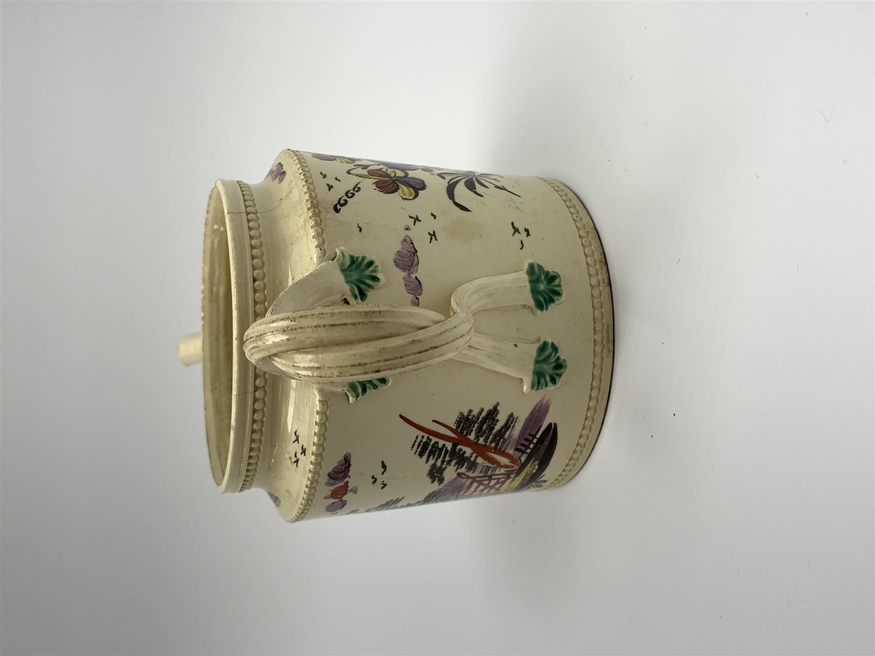 18th century creamware teapot, probably Leeds, with reeded entwined handle and floral finial to the cover, the body with hand painted polychrome decoration of figure to one side, and floral spray to the other, collectors paper label beneath inscribed Leeds Pottery, H11.5cm