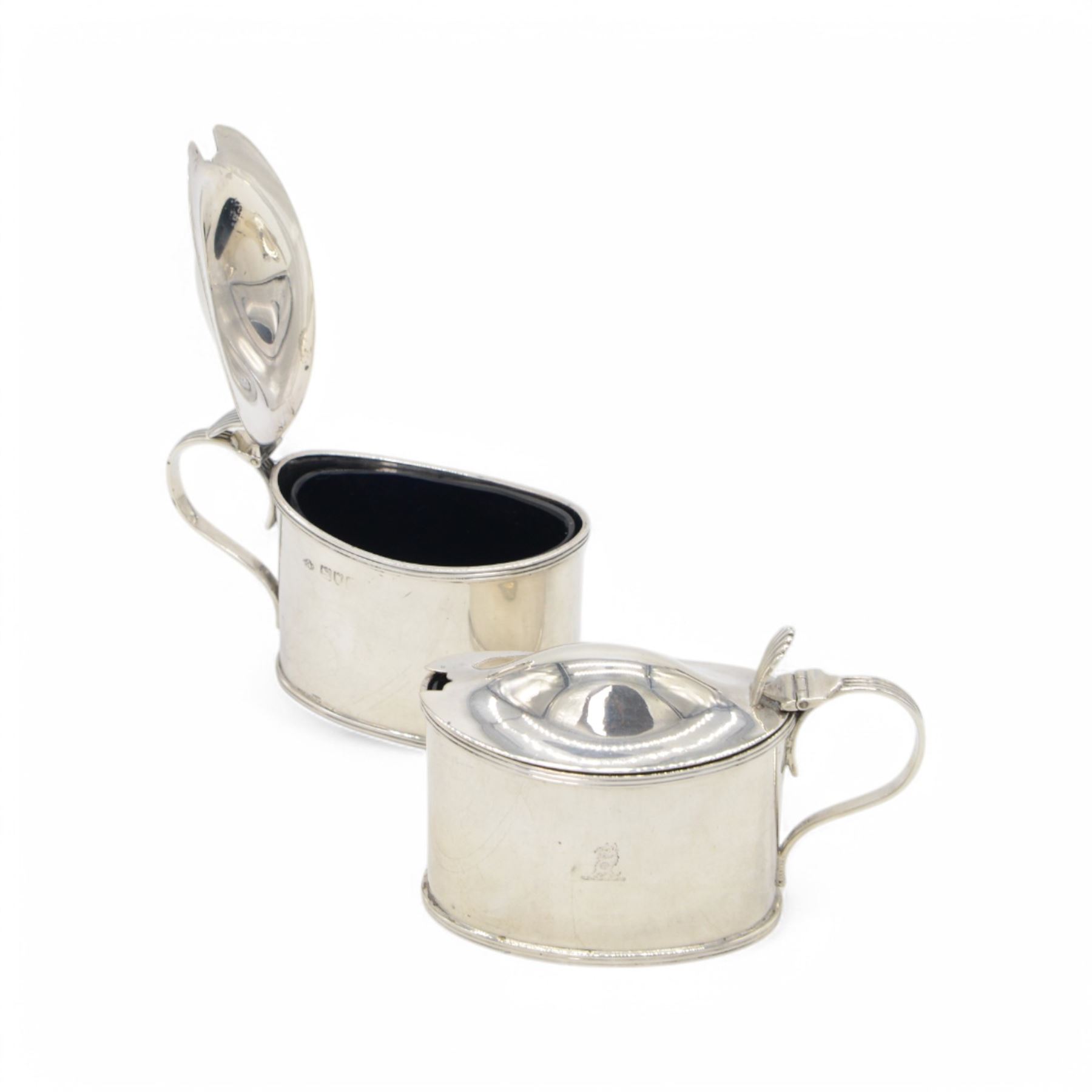 Pair of Edwardian silver mustard pots, of oval form with reed borders and palmette thumb pieces to hinged covers, opening to reveal blue glass liners, hallmarked William Hutton & Sons Ltd, London 1905, H7.5cm