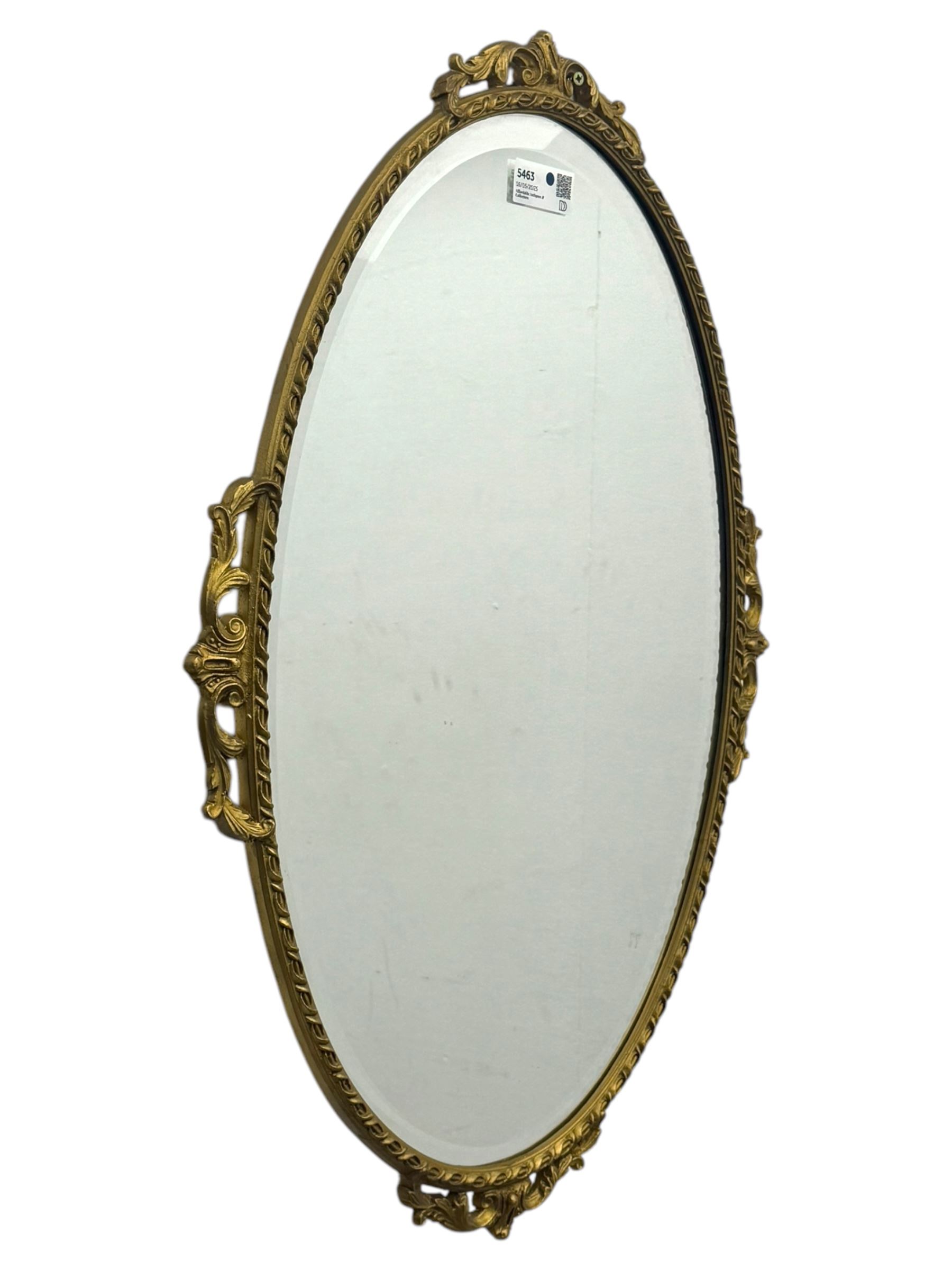 Oval gilt wall mirror, with bevelled edge plate within a moulded frame cast with acanthus scrolls and foliate decoration, pierced cartouche crest and apron, flanked by scrollwork handles