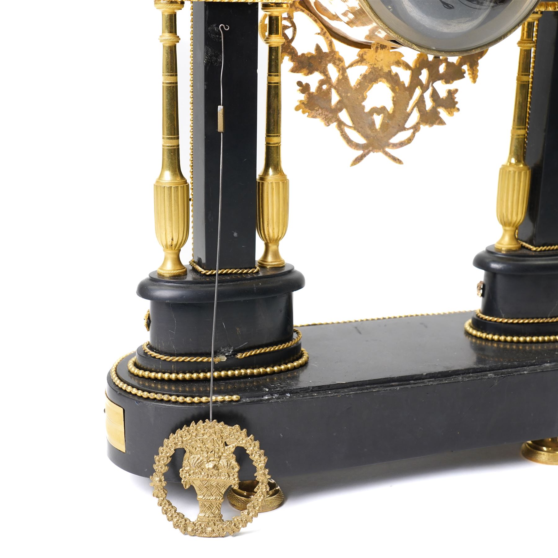 French-Early 19th century 8-day ormolu and polished black slate portico clock, case surmounted with a twin handled urn with flowers, supported by two square pedestals with finials and trailing floral mounts on oval bases, raised on an oval plinth with toupie feet, enamel dial signed 