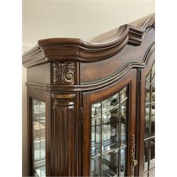 Kevin Charles American walnut display cabinet, illuminated interior, shell carved pediment above four bevel edge doors enclosing six glazed shelves above one central long drawer flanked by two short drawers, above three cupboards, carved bracket supports 