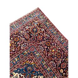 Large Persian Kashan crimson ground carpet, large floral central medallion surrounded by trailing branches decorated with leaves and stylised plant motifs, the main border with scrolling design interspersed with palmettes, within floral pattern guard stripes 