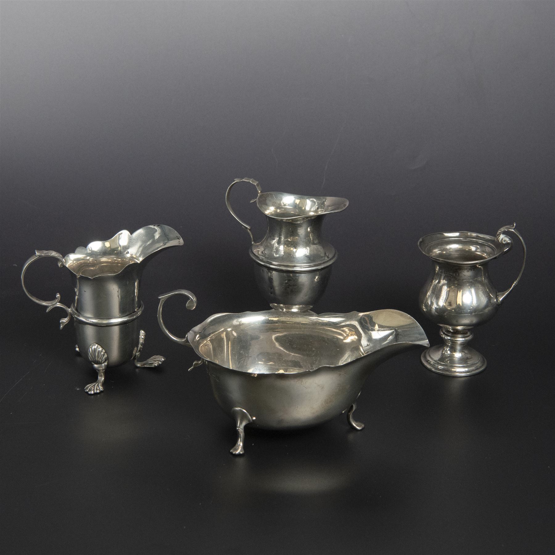 Group of early 20th century silver, comprising sauce boat, with flying scroll handle and upon three pad feet, two small cream jugs and a christening mug, all hallmarked, tallest H10cm