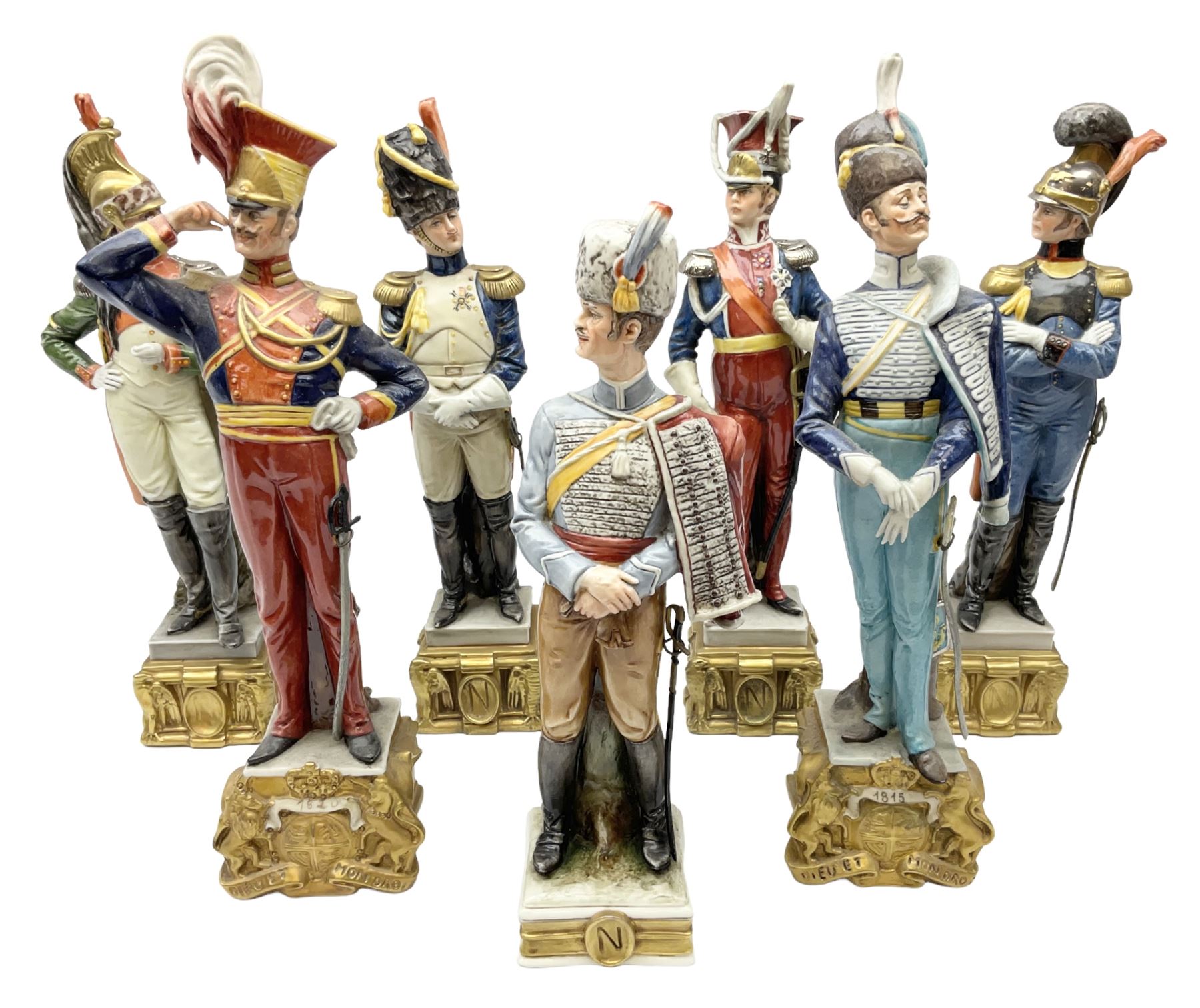 Group of seven Capodimonte figures of soldiers, to include four Bruno-Merli examples including Officer of the 12th Lancers 1820 and Captain of the 18th Hussars 1815, both raised upon ornate gilt plinths bearing British monarch motto in Latin 'Dieu et mon droit', and three further similar, all with crowned N mark beneath, tallest H32cm