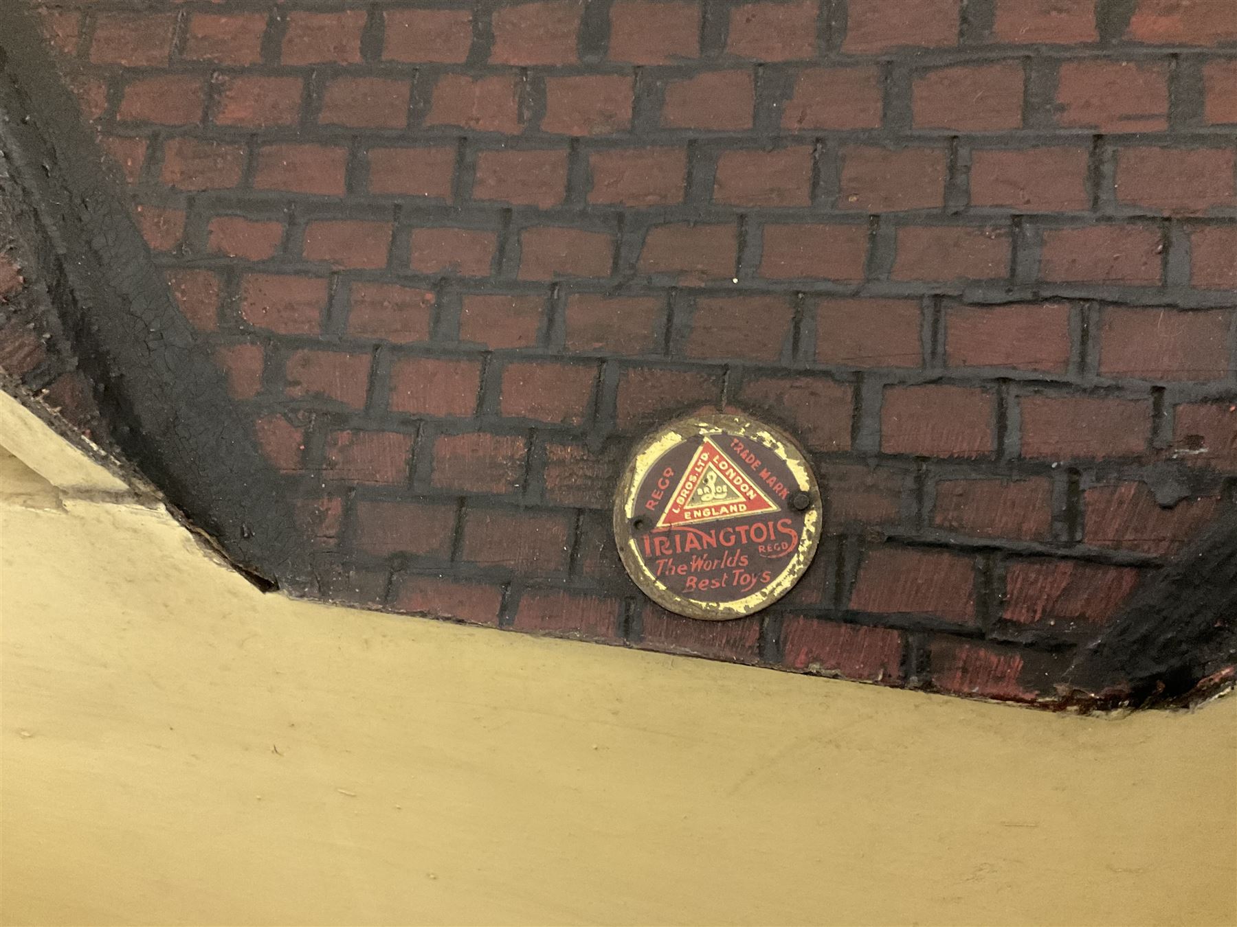 Large Tri-ang No.93 doll`s house in the 'Stockbroker's Range' c1935; two-storey double-fronted Tudor design, half timbered gables, two-storey bay windows, cream and mock shrubbery to front, opening metal framed windows with green shutters, red simulated tiled roof with chimney, integral garage with opening doors, front elevation has four hinged doors opening to reveal two bedrooms with fire places, living room, bathroom and kitchen with built in dresser and sink, entrance hall and staircase, side entrance with porch and seat and sun dial over on chimney stack; some wiring for electrical lighting; metal Tri-ang Toys disc verso; comprehensively furnished H66cm L117cm D43cm