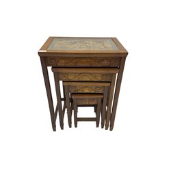 Mid-20th century nest of four Singapore hardwood tables, glass topped insets carved with traditional scenes of figures, carved frieze with landscape design on square tapering supports