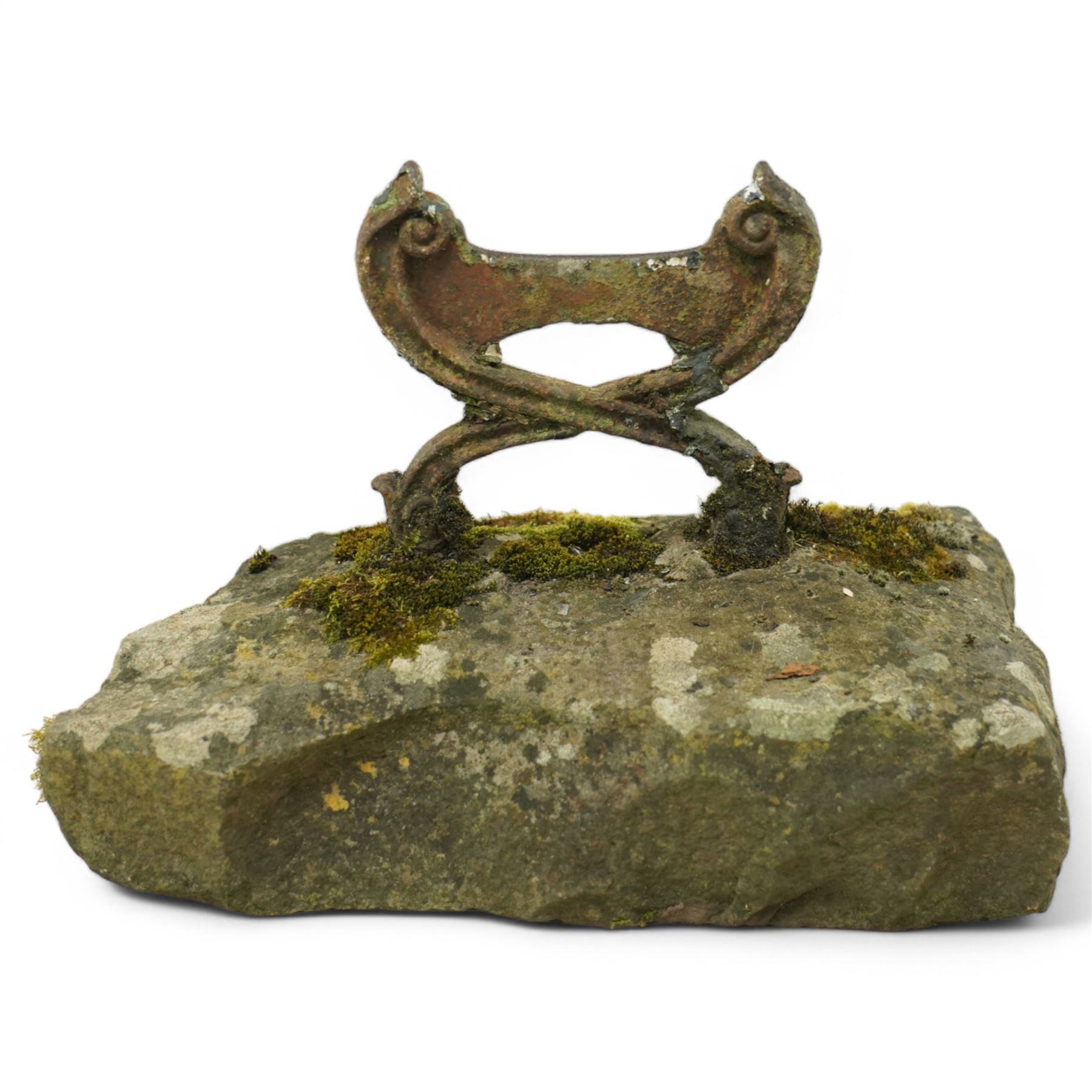 19th century cast iron boot scraper, with scrolled upright mounts, set into a rectangular moss-covered stone base