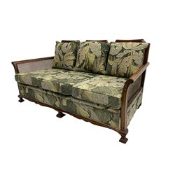 Early 20th century bergère lounge suite, mahogany framed with cane work back and sides, acanthus scroll carved uprights - three seat sofa (W167cm, H82cm, D83cm), and pair matching armchairs (W78cm), loose cushions upholstered in acanthus leaf scroll fabric with scatter cushions