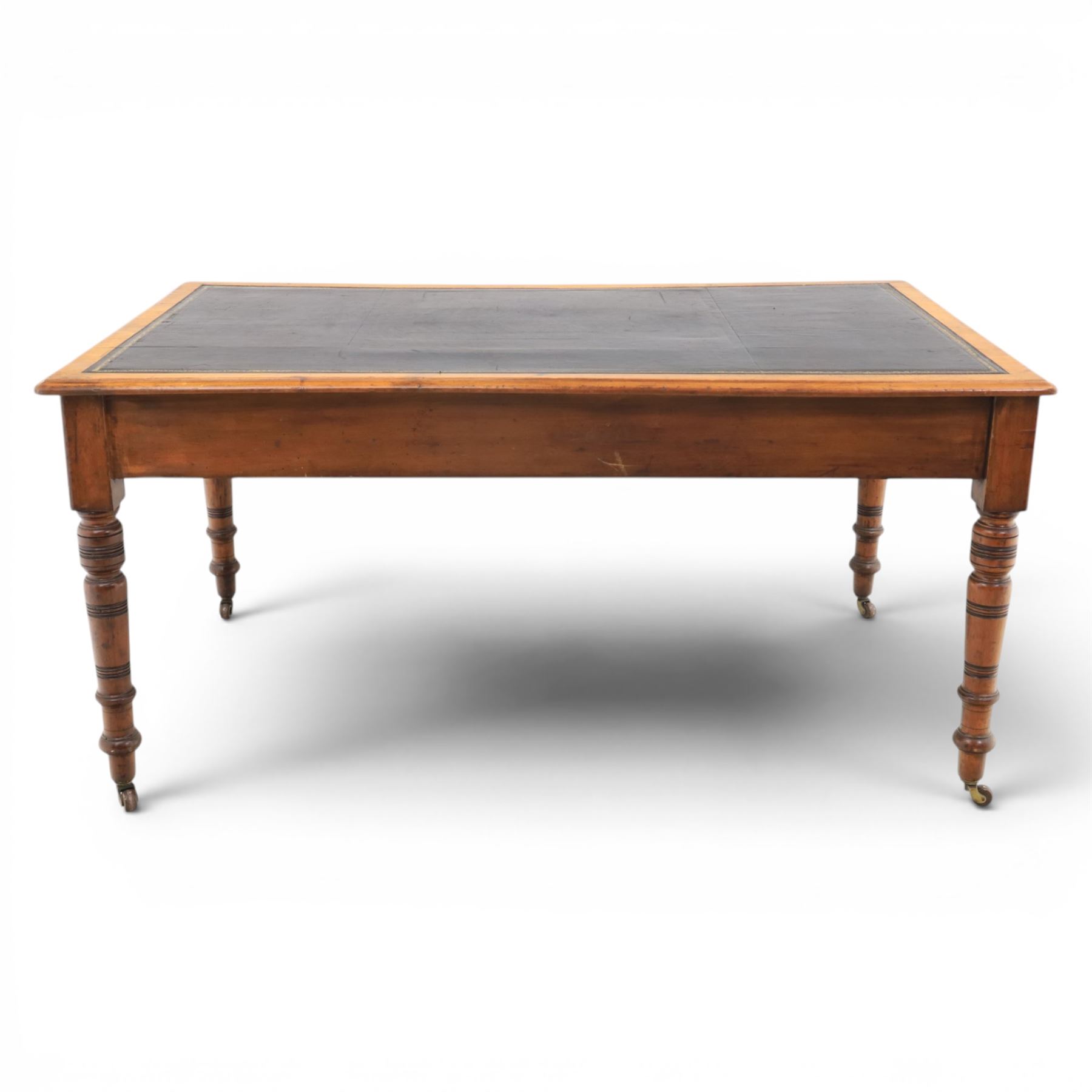 Victorian pitch pine writing table with leather inset top, rectangular top with three frieze drawers, pierced brass handles, raised on turned and fluted supports terminating in castors