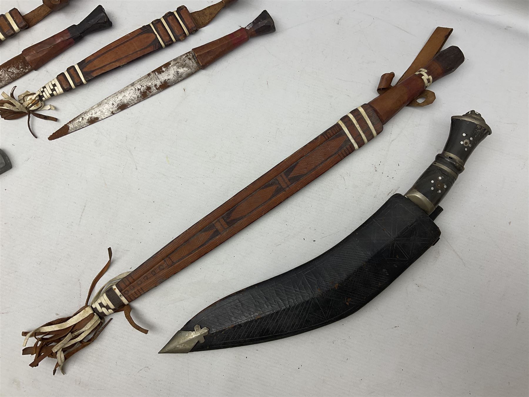 Indian kukri with 29cm curving steel blade and nickel mounted horn grip; in leather covered scabbard with one skinning knife L42cm overall; Hitler Youth knife with scabbard in relic condition; and three African graduated knives each with crudely carved wooden grips and painted leather covered scabbards (5)