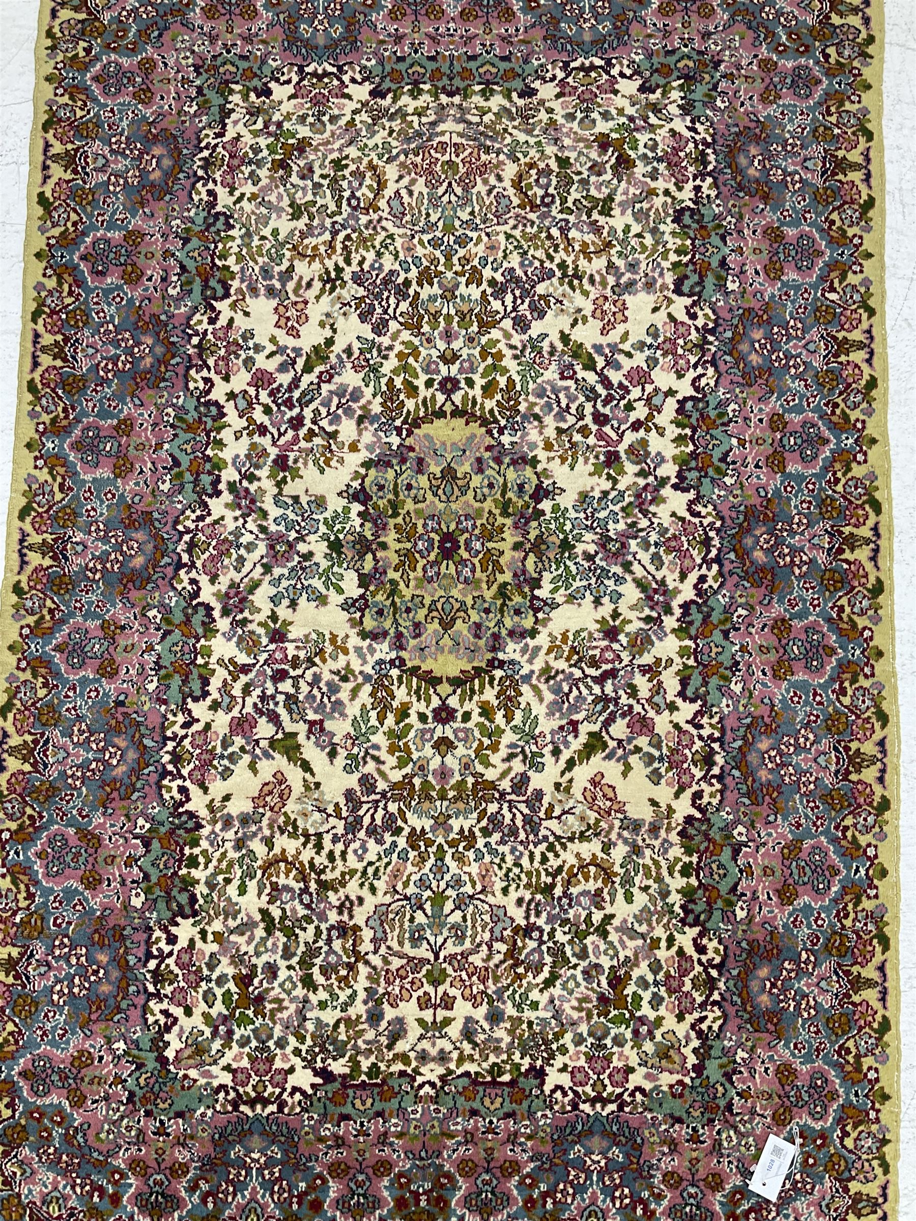 Central Persian Kirman ivory ground rug, decorated all-over with flower heads and trailing foliage, shaped pink and blue ground borders with olive green outer band