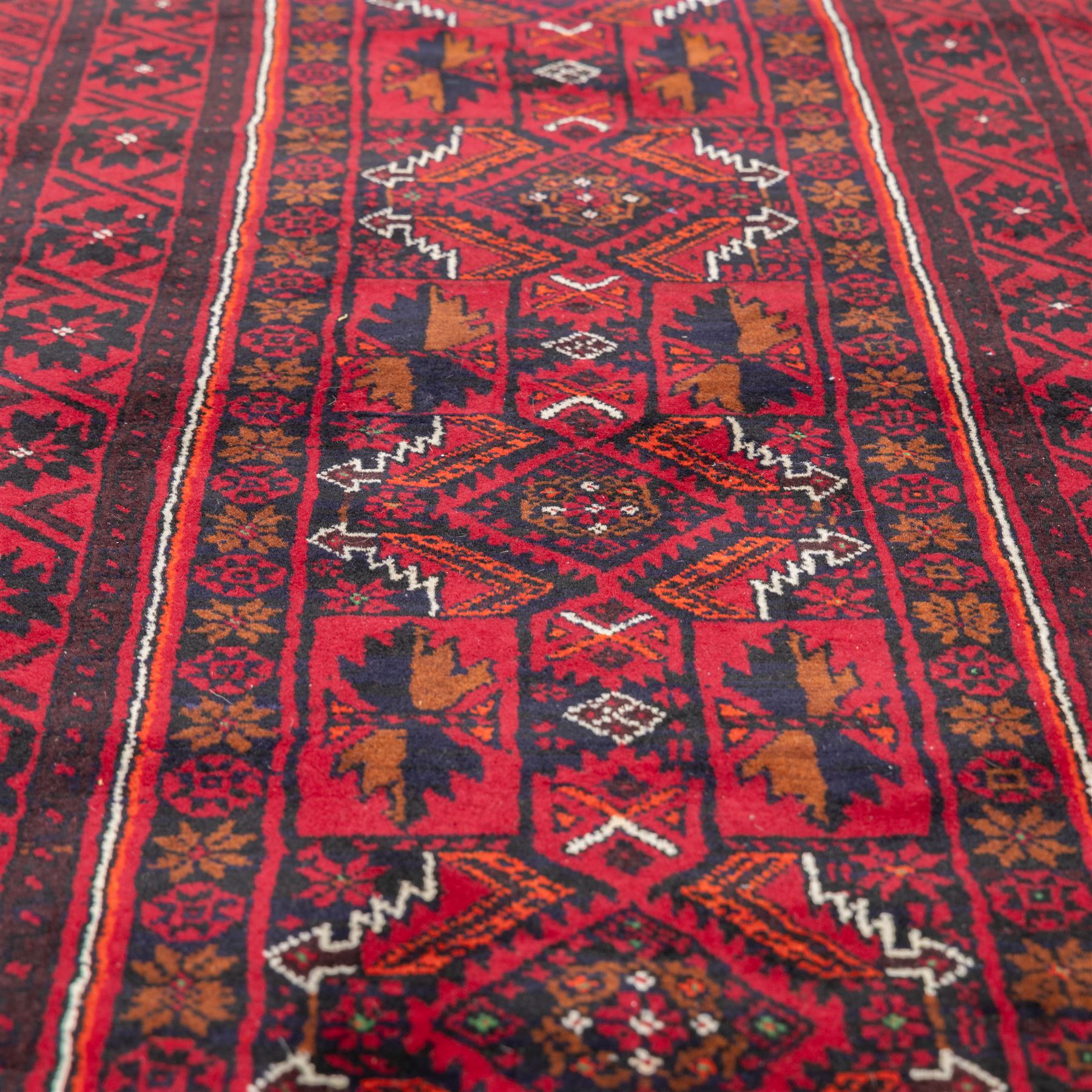 North east Persian Baluch hand-knotted runner, crimson ground with a vertical column of hooked lozenge medallions flanked by stylized leaf motifs within multiple geometric borders of rosettes and angular vines  
