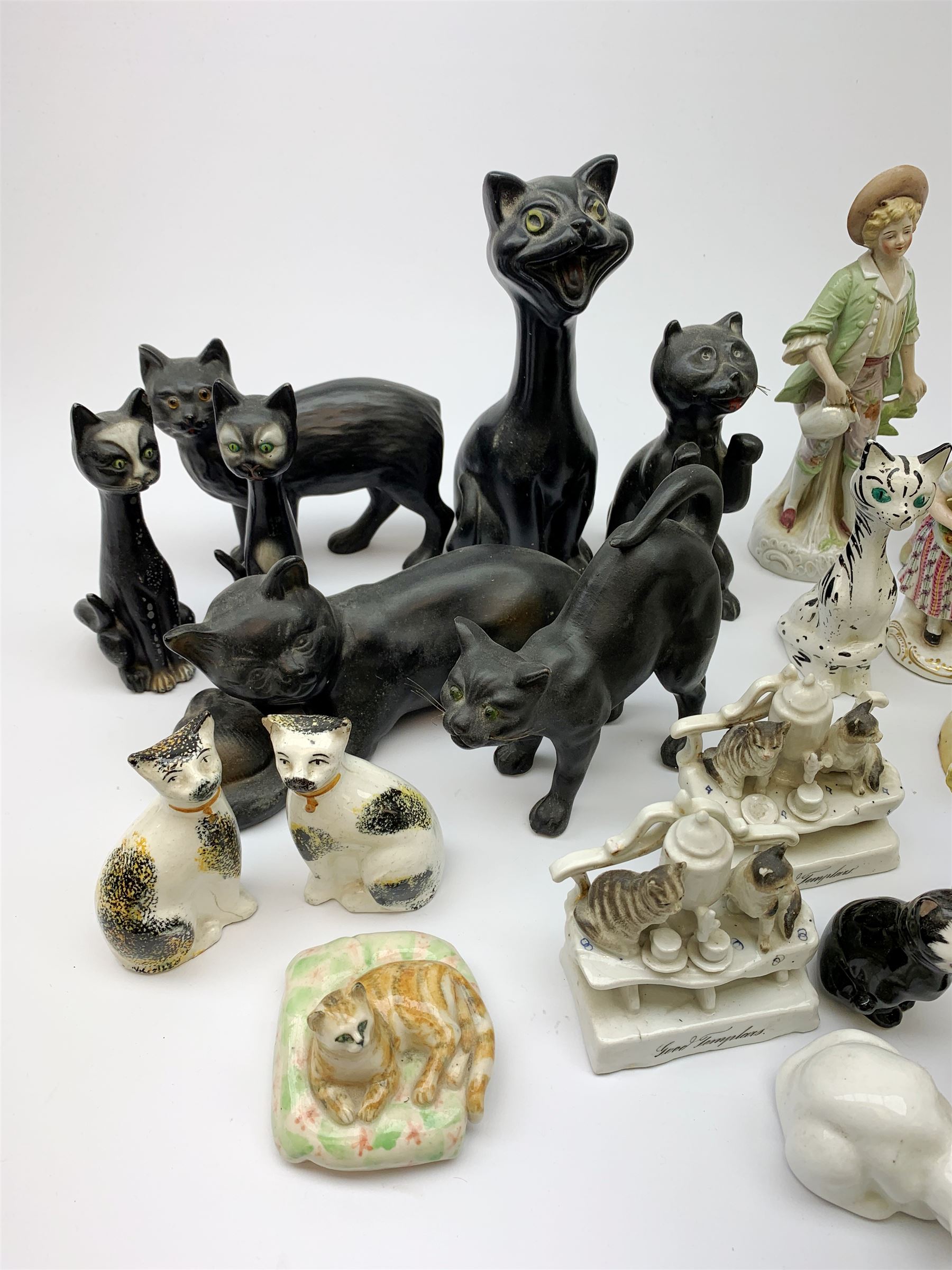 A collection of various ceramic figurines, to include pair of small 19th century Staffordshire cats, Royal Doulton cat, Coalport cat, pair of 19th century pug dogs, two fairings inscribed Good Templars, two Bonzo dog peppers, a number of pin cushion dolls, various 20th century and later black pottery cats, Victorian bisque figures, etc. 