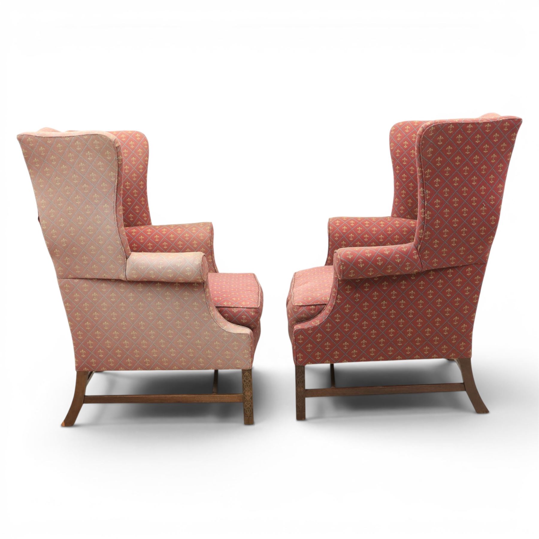 Georgian design wingback armchairs, the high backs flanked by shaped wings over padded scroll arms, upholstered in burgundy and gilt fleur-de-lys patterned fabric, loose cushion seats, raised on square tapering front supports