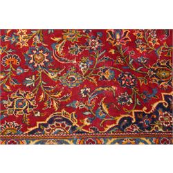 Persian Kashan hand-knotted carpet, madder red ground centred by shaped dark navy, ivory and pale blue floral medallion with pendants, surrounded by scrolling vines, palmettes and flowerheads, dark navy spandrels, enclosed by dark navy floral border with multiple floral guard stripes