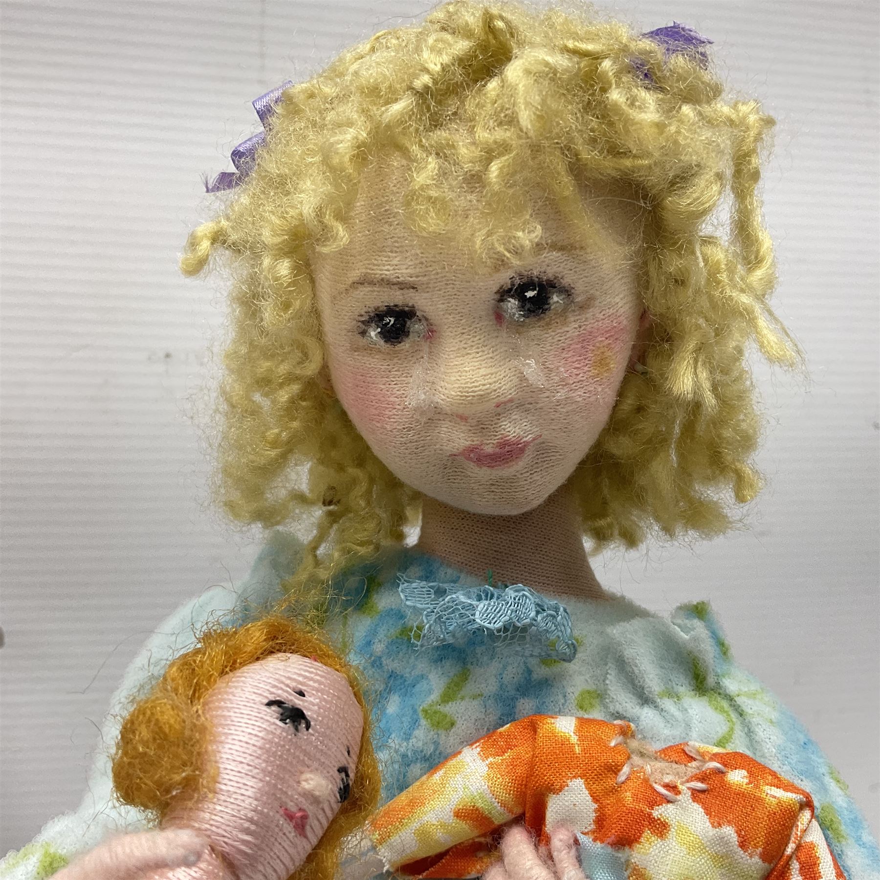 Anna Meszaros Hungary - three hand made needlework figurines - 'The Cobbler' as a child seated in a wooden rocking chair working on a removed boot H24cm; young girl standing crying holding a doll with broken head H32cm; and young girl in long dress and bonnet standing holding a doll H27cm (3)  Auctioneer's Note: Anna Meszaros came to England from her native Hungary in 1959 to marry an English businessman she met while demonstrating her art at the 1958 Brussels Exhibition. Shortly before she left for England she was awarded the title of Folk Artist Master by the Hungarian Government. Anna was a gifted painter of mainly portraits and sculptress before starting to make her figurines which are completely hand made and unique, each with a character and expression of its own. The hands, feet and face are sculptured by layering the material and pulling the features into place with needle and thread. She died in Hull in 1998.