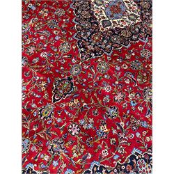 Persian Kashan crimson ground carpet, floral pattern indigo ground central medallion and matching spandrels, the field decorated densely with scrolling foliate patterns and floral motifs, the main border decorated with scrolling branches and palmettes, within floral pattern guard stripes