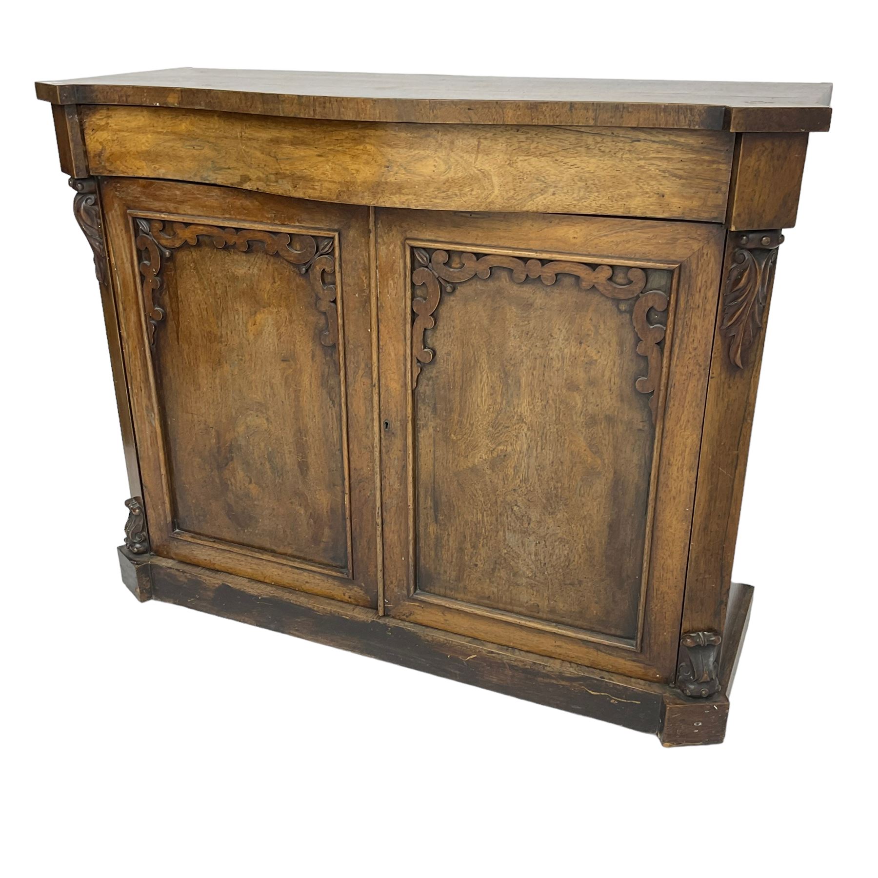 William IV rosewood serpentine chiffonier, fitted with frieze drawer over two panelled cupboard doors with applied C-scroll decoration, flanked by canted uprights with moulded foliate corbels