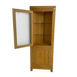 Light oak corner display cabinet, single glazed door enclosing two glass shelves, over single cupboard