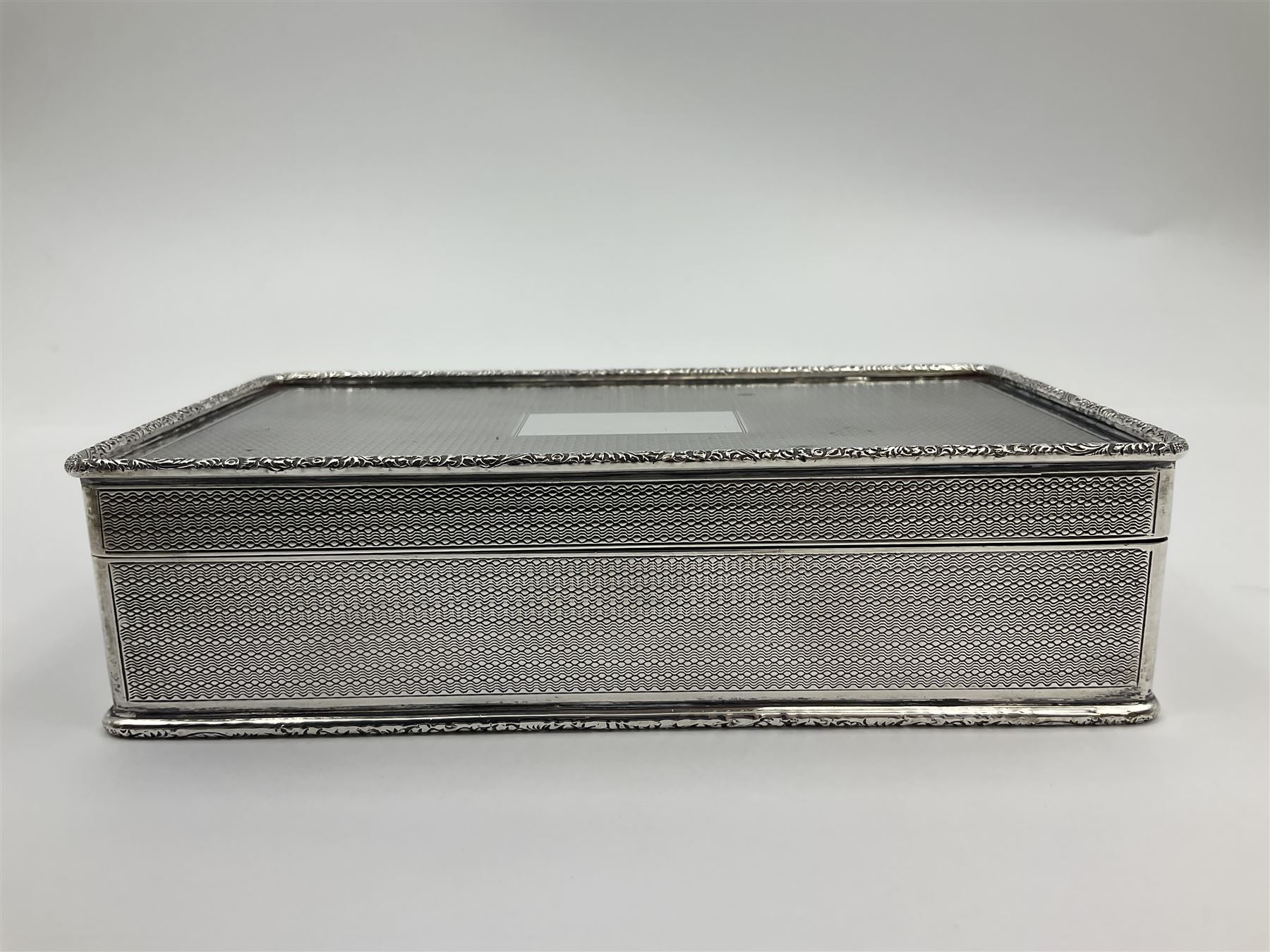 1920's silver table cigarette box, of rectangular form with engine turned decoration to the exterior, the hinged cover with central vacant rectangular panel and raised foliate rim, opening to reveal a gilt interior with later plush lining, hallmarked Charles Henry Dumenil, London 1923, H3.5cm L14.5cm D8.5cm