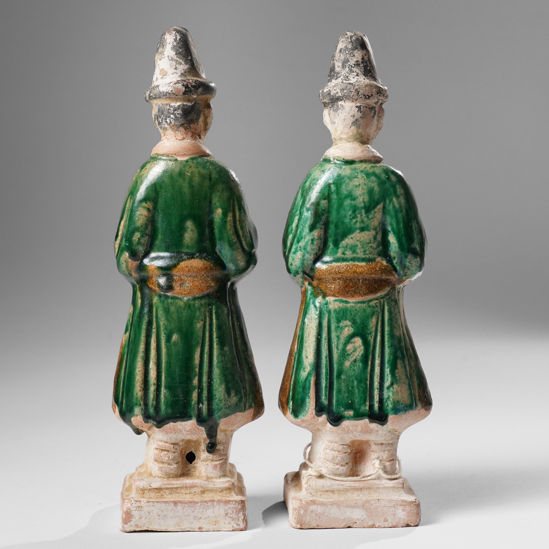 Pair of Chinese terracotta court attendant tomb figures,  probably Ming Dynasty, in Sancai green glaze, upon stepped square bases, H22cm 