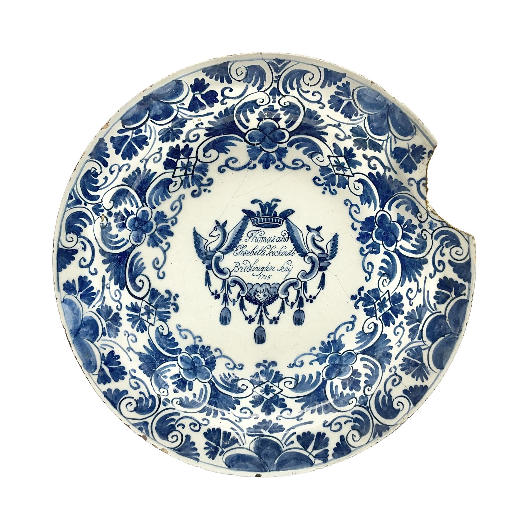 Early 18th century Delft marriage plate, of circular form with dished centre, the centre inscribed and dated 'Thomas and Elizabeth Kockerill Bridlington Key 1715' within a crowned C scroll cartouche, flanked by demi-griffins, above a putto head and tassels, within a wide foliate border, D34cm

