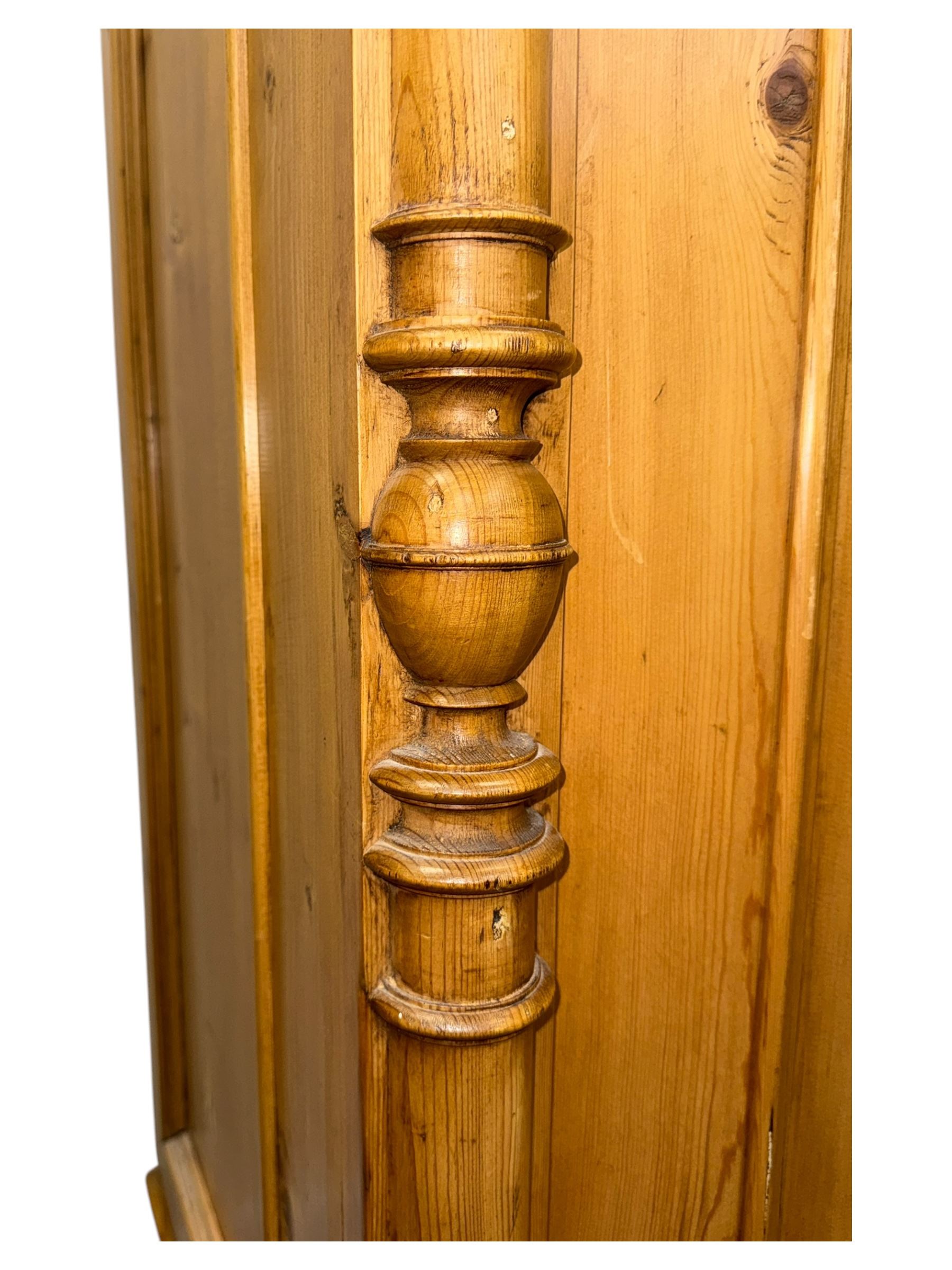 Large 19th-century Continental polished pine double wardrobe, panelled back and doors revealing brass hanging rod, flanked by half-turned columns with Corinthian capitals supported on bun feet