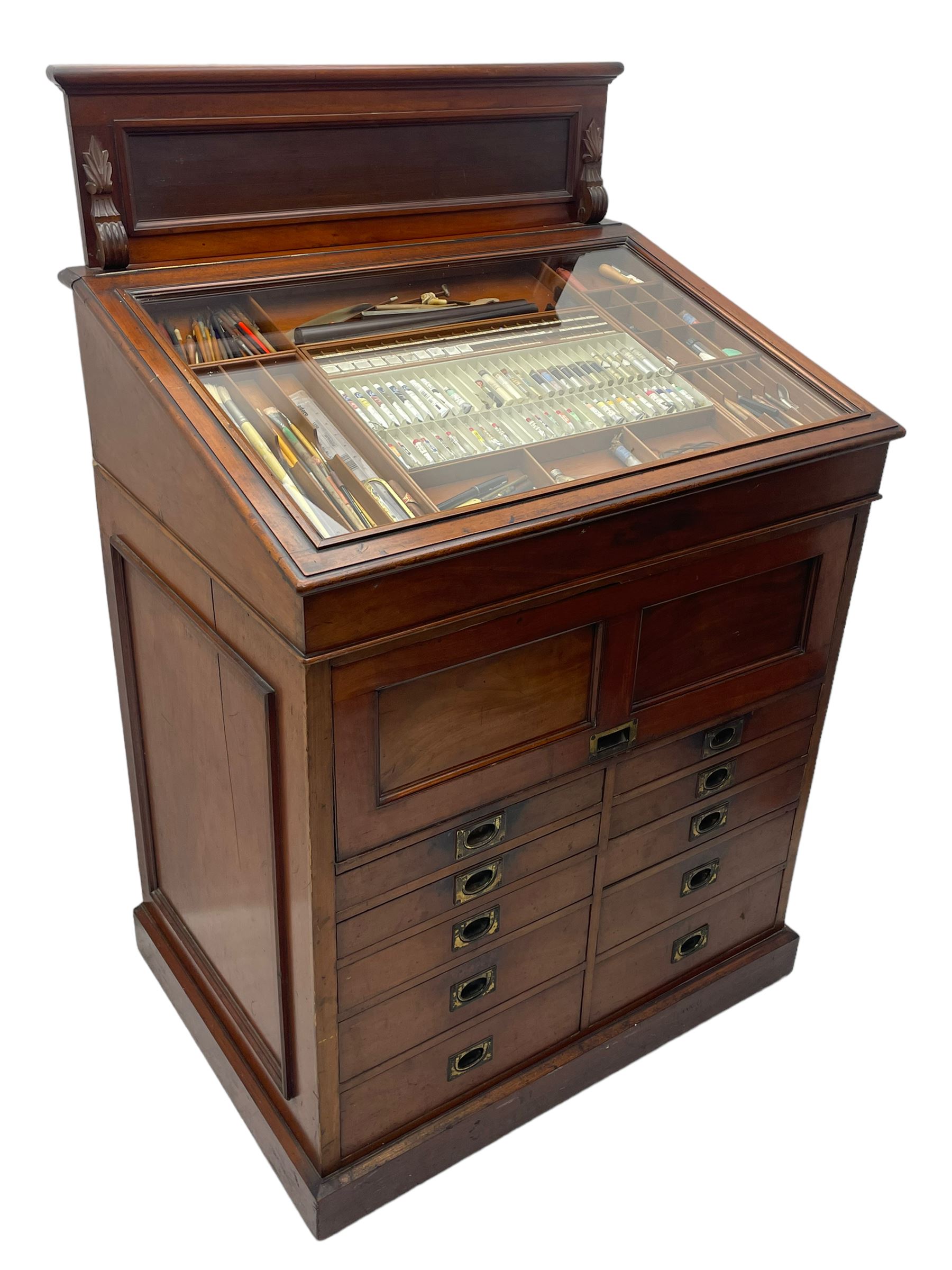 Edwardian mahogany artist's cabinet once belonging to the British artist Eli Marsden Wilson (1877-1965), raised panelled back mounted by carved brackets, sloped and hinged glazed lid enclosing paint holders and compartments, up-and-over panelled door revealing three slides, fitted with two banks of five graduating drawers with recessed brass handles, on skirted base.

Together with a quantity of artists' equipment and tools including paints, paintbrushes, charcoal, chalks, etc. and various prints relating to the life of the artist, including Quaker anti-war posters, Victorian Stevengraphs, and various chromolithographs 

Provenance: Removed from the studio of Eli Marsden Wilson. The cabinet comes to us for sale through family descent. The vendor is descendant of Marsden. Many further etchings removed from the cabinet are being sold in the Spring Art Sale, Friday 15th March 2024, Lots 265-271.

Notes: born in Ossett, Eli Marsden Wilson was the only son of Alfred Wilson, a foreman beamer, and Emma Marsden, and had five sisters. After studying at Wakefield College of Art, he moved to the Royal College of Art in London, where he became a pupil of Sir Frank Short. He had his first exhibit at the Royal Academy in 1905, the same year he married fellow artist Hilda Mary Pemberton.

A Quaker, vegetarian, and pacifist, he was a conscientious objector in World War I and as such was imprisoned in 1917 for two years. In September 1922 he was commissioned by Princess Marie Louise to produce miniature etchings for Queen Mary's Dolls' House at Windsor Castle; two such etchings are being sold in the Spring Art Sale, Friday 15th March 2024, Lot 265.