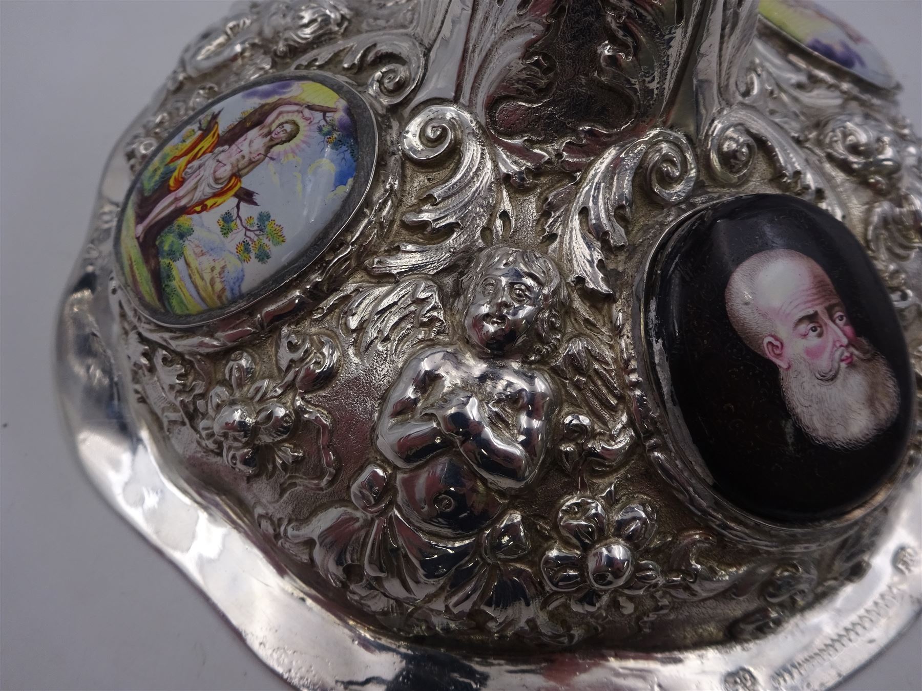 German silver chalice, the bowl, stem and foot each with 19th century repousse and chased decoration depicting putti masks, C scrolls and flowers, set with two hand painted porcelain roundels, possibly Berlin, and six later applied enamel roundels, each depicting religious scenes, the gilded bowl upon knopped stem and spreading octofoil foot, the base with marks for Munich, c.1695 and maker's mark FK