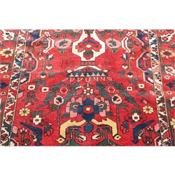Vintage Persian Heriz crimson ground rug, the field decorated with a central stylised urn and bird of paradise motifs, the guard  lines with repeating stylised plant motifs of geometric form