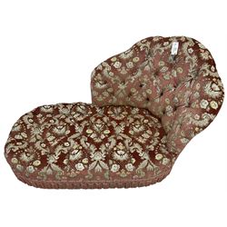 Early 20th century small chaise longue, scallop shaped back over sprung seat, upholstered in buttoned foliate patterned pink velour fabric with fringing, on turned supports with castors
