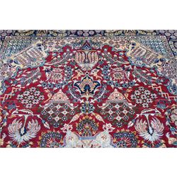 Central Persian Najafabad hand-knotted carpet, crimson field with a central elaborate cusped medallion with radiating floral motifs, surrounded by finely drawn scrolling vines incorporating stylized palmettes and rosettes, flowering plants and vase motifs, ivory spandrels similarly decorated enclosed by a dark indigo main border of floral arabesques between multiple guard stripes, with cotton fringe ends 