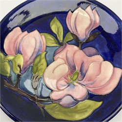 A Moorcroft plate decorated in the magnolia pattern upon a dark blue glazed ground, with impressed and painted marks beneath, D26cm. 