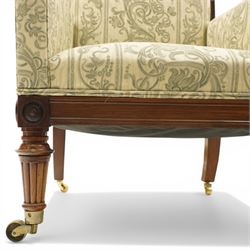 William IV rosewood framed library armchair, squared form with green on ivory ground upholstery, moulded lower seat rail with applied roundels over reeded supports, terminating to brass cups and castors