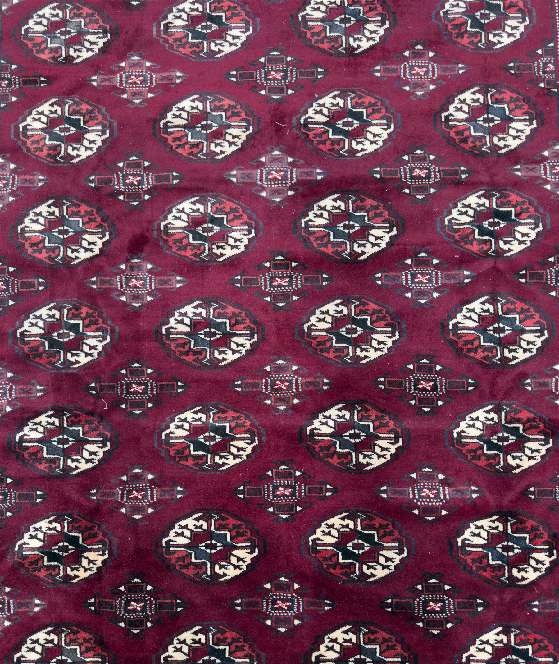 Northeastern Persian Yamut  hand-knotted carpet, the rich burgundy field with repeating rows of stepped gul motifs in cream and black, enclosed by multiple linear and geometric borders with hooked motifs and diamond medallions