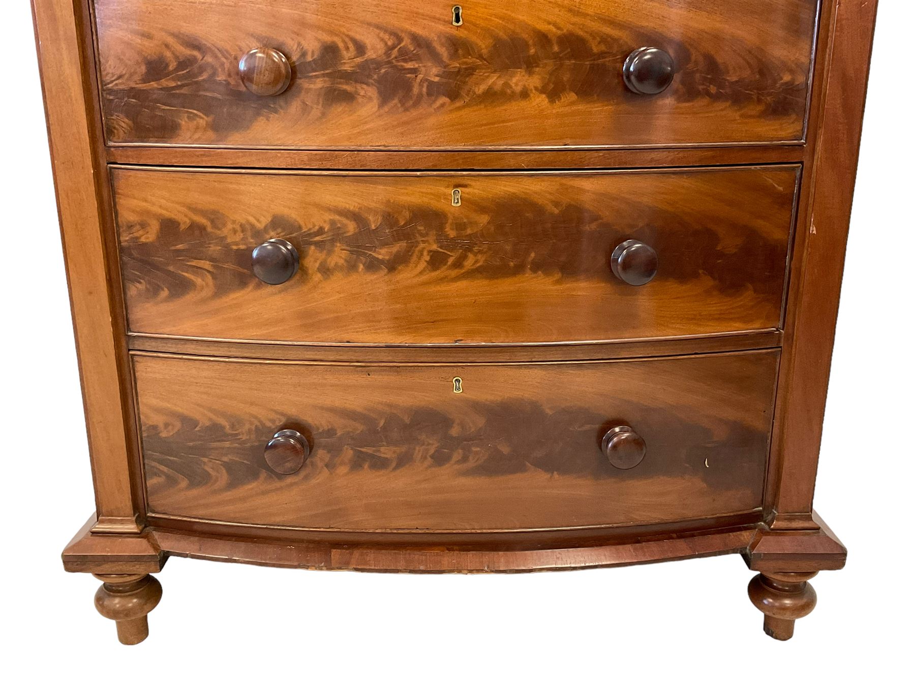 Late 19th century mahogany bow-front chest, fitted with banded cushion drawer with secret catch, above two short over three long graduating drawers, each cock-beaded with turned handles, lower moulded edge over turned feet