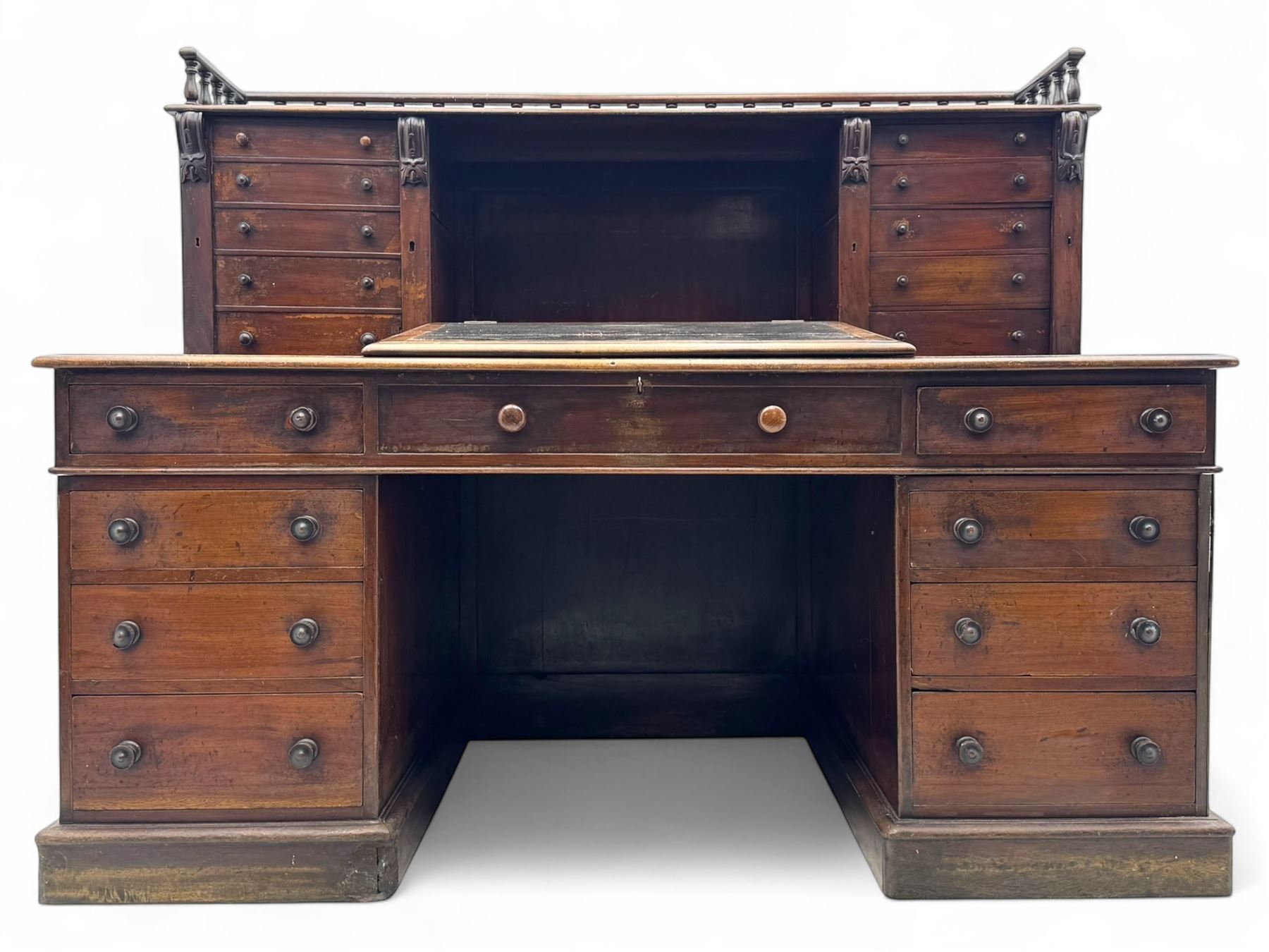 Large Victorian mahogany Registry/Dickens’ desk, spindle gallery top, one side with five small drawers and the other with blind cupboard drawer, revealing pigeon holes with scroll carved locking side bars on either side, above a hinged and leathered writing slope with three drawers and pigeon holes underneath, above a central locking drawer with key, the pedestals each with four drawers and  turned knob handles, separates into four parts for transport