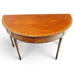 Georgian mahogany demi-lune card table, the lunette shaped top with cross-banded and boxwood-strung edge, opening to reveal baize-lined interior and supported by rear gatelegs, over a banded frieze with applied oval plaques, raised on turned and tapering supports