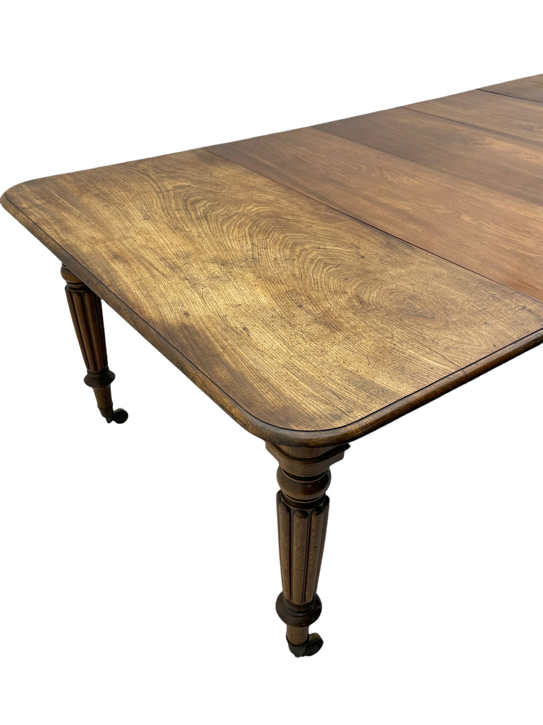Early 19th century figured mahogany extending dining table, the rectangular top with moulded edge and rounded corners, pull-out action with three additional leaves, raised on turned and lobe carved supports with brass cup castors