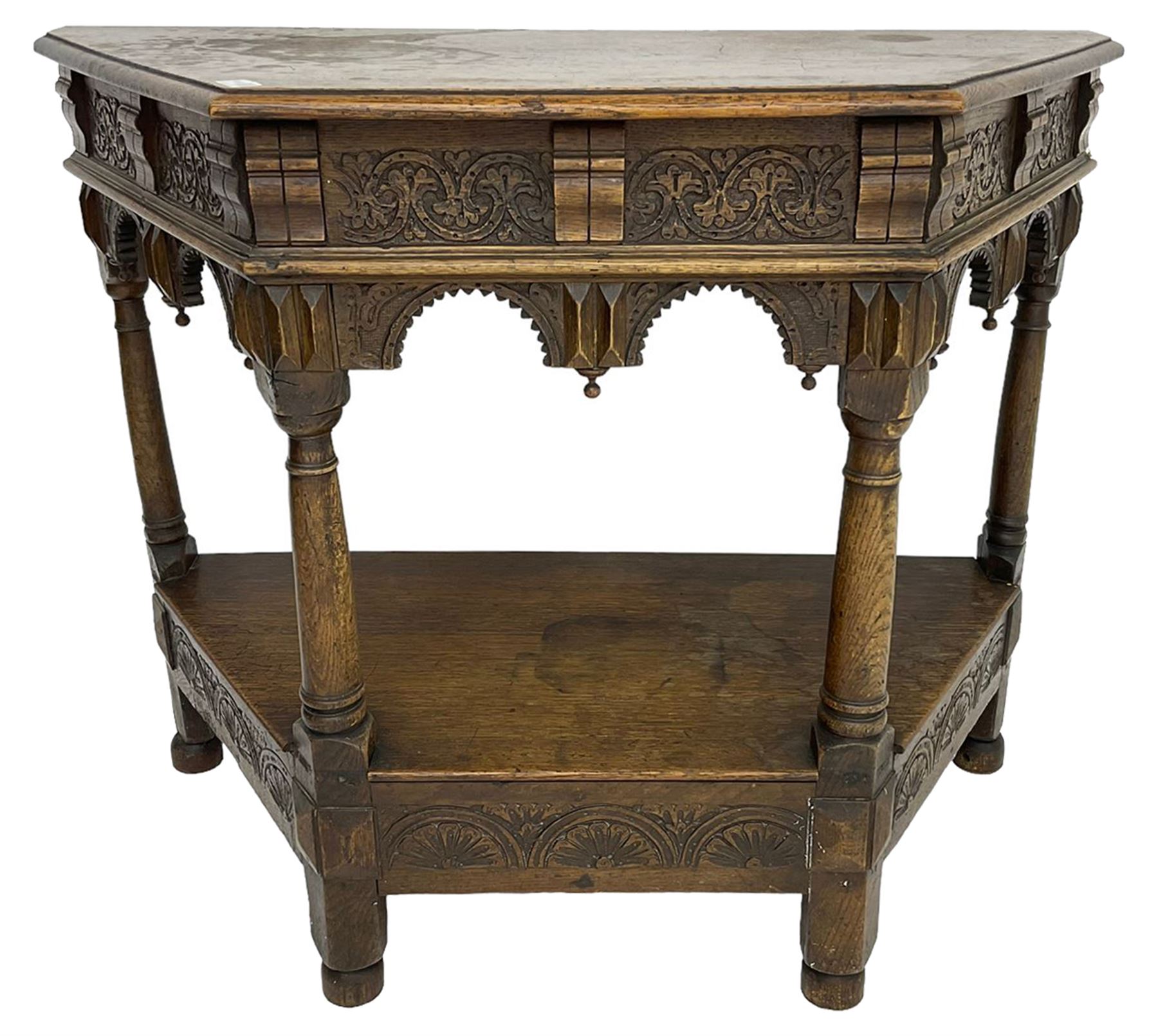 Jacobean design carved oak side or credence table, demi-heptagon top with moulded edge, frieze carved with foliate C-scroll design above ornate arcade carved apron, under-tier united by ring turned pilisters, lower frieze carved with repeating lunettes