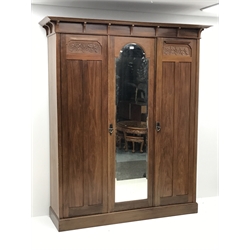 Irish Arts & Crafts walnut triple wardrobe circa 1908, projecting cornice above three doors enclosing fitted interior, single full length bevel edge mirror, platform base, W173cm, H204cm, D56cm
