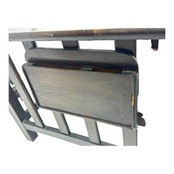 Late Victorian oak steamer chair, adjustable slatted backrest with grooved crest rail, wide armrests extending to a sliding adjustable footrest, open frame sides with vertical slats, side magazine rack and collapsible table, raised on turned front supports