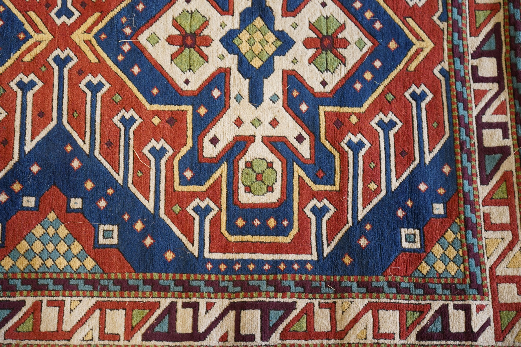 Caucasian Kazak indigo and vermillion ground rug, the geometric field boldly woven with two medallions interspersed with symbolic tribal motifs and shapes, with contrasting ivory guard band