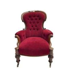 Victorian mahogany armchair, scroll carved cresting rail and uprights, upholstered in buttoned red fabric, turned and lobe carved front feet with brass castors