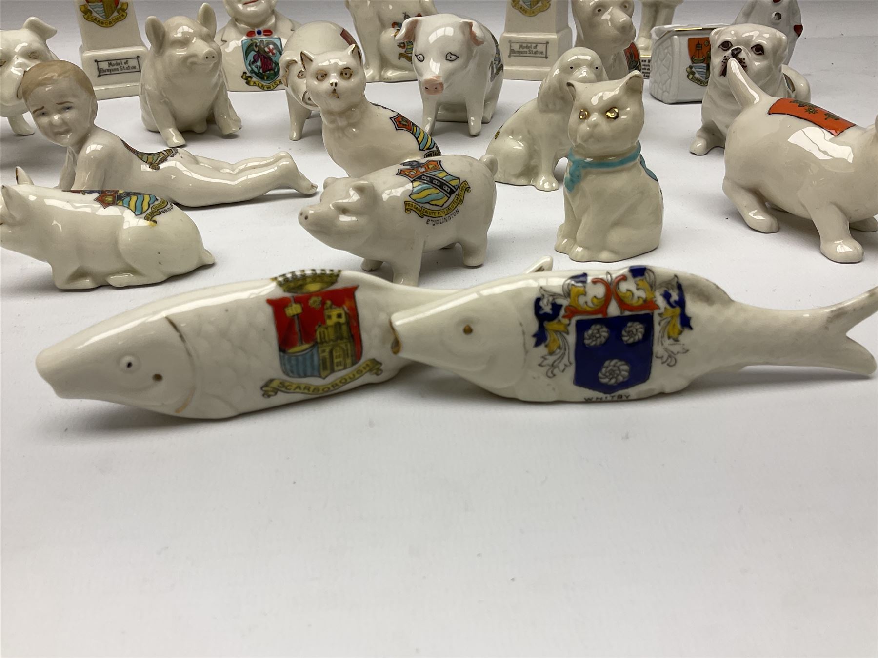 Collection of figural crested ware, to include Carlton Chins John Bull Alnwick, Clifton China Cheshire Cat,  Arcadia pig, Crafton crawling baby and another seated baby, quantity of cat, dog and pig figures, two Willow Art Model of Bunyans Statue, Toby jug, Victoria China, Arcadan bulldog, fish etc